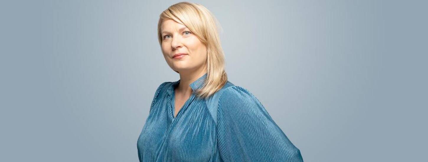 Portret van Cecilia Moisio gekleed in blauwe jurk en handen in haar zij.