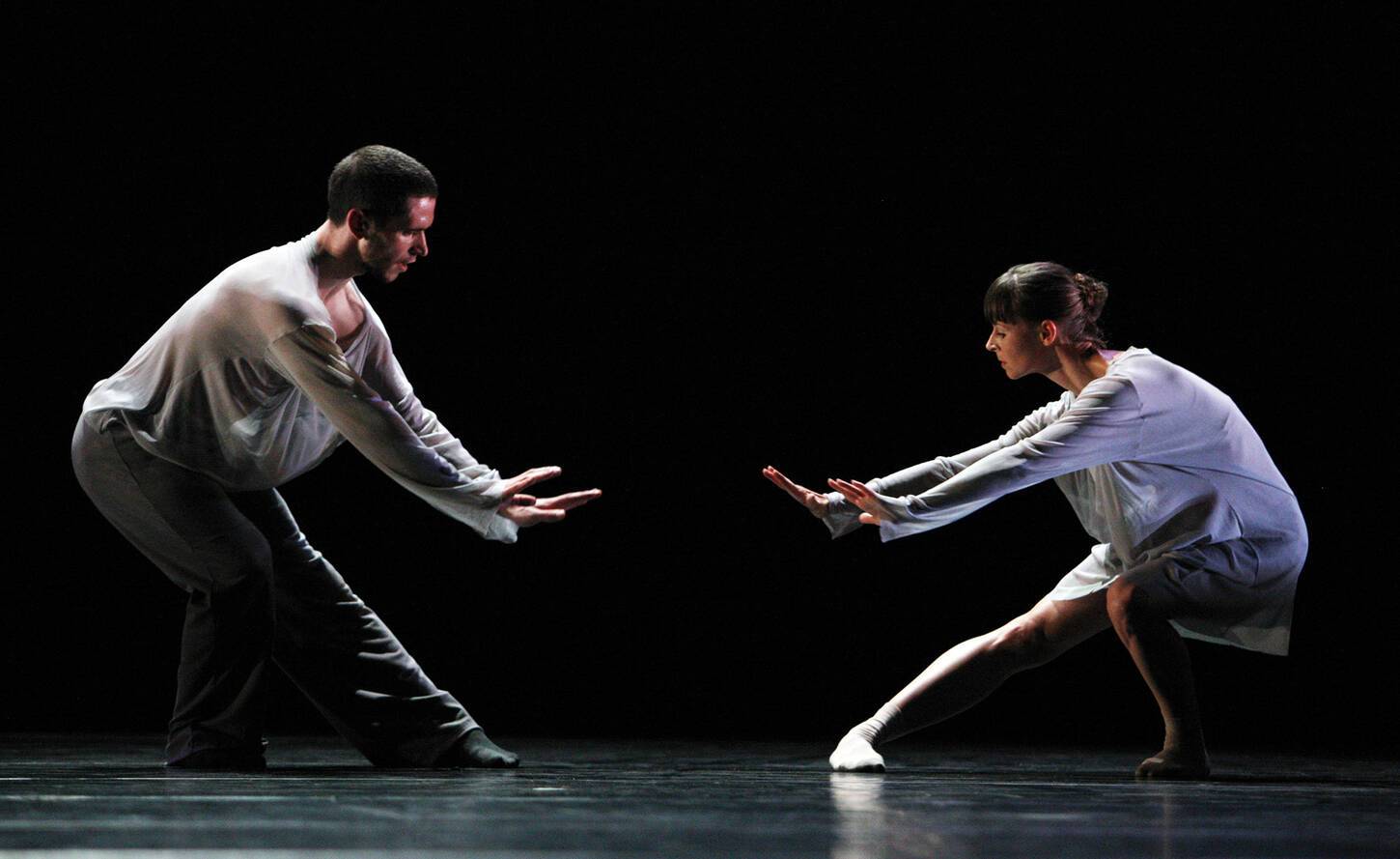 Twee dansers in duet door de benen gebogen met de armen vooruit gestrekt