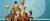 Een familie is te zien op een bruine bank voor een blauwe achtergrond. De familie kijkt in de camera. Naast de familie staat een dame met grote pruik, zonnebril, oranje hakken, lichtblauw mantelpak en een roze huid. 